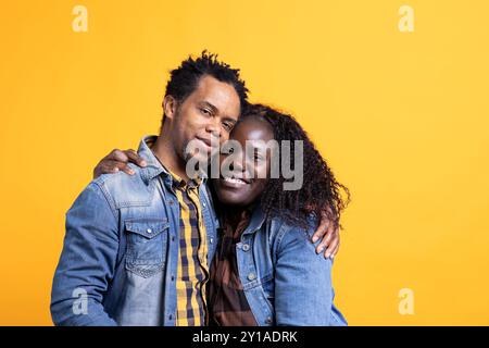 Liebe afroamerikanische Ehemann und Ehefrau, die sich im Studio umarmt, lächelt und verliebt vor gelbem Hintergrund ist. Positive, freudige Lebenspartner, die sich mit Leidenschaft und Zuneigung umschließen. Stockfoto
