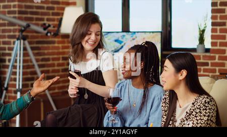 Die besten Freunde lachen zusammen, genießen alkoholische Getränke und Gourmet Käseplatte im gemütlichen Wohnraum. BIPOC Gruppe von Leuten, die zu Hause lebhafte Gespräche führen und sich unterhalten Stockfoto