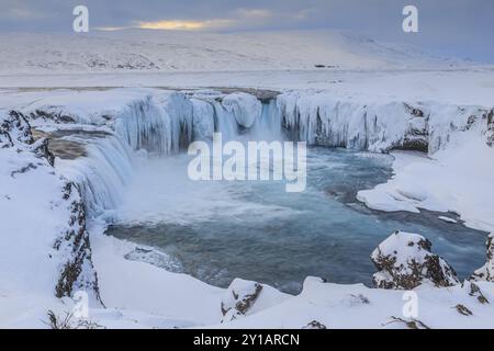 Eisiger Wasserfall und Stromschnellen vor einer Berglandschaft, bewölkte Stimmung, Schnee, Godafoss, Island, Europa Stockfoto