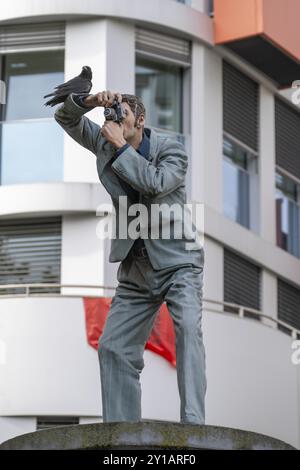 Echte Krähe auf einem Säulen-heiligen, der Fotograf, vor dem Hauptbahnhof in Düsseldorf, eine von 10 realistischen, lebensgroßen Skulpturen von Menschen Stockfoto