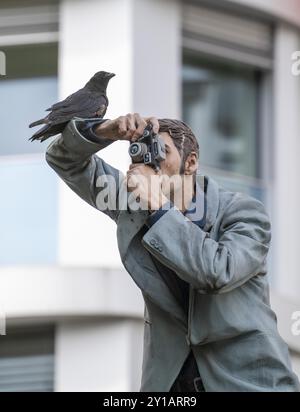 Echte Krähe auf einem Säulen-heiligen, der Fotograf, vor dem Hauptbahnhof in Düsseldorf, eine von 10 realistischen, lebensgroßen Skulpturen von Menschen Stockfoto