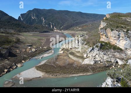 Ein sich windender Fluss durchquert felsige Landschaften und grüne Hügel, umgeben von steilen Bergen unter klarem Himmel, Noguera Ribagorcana Mont-rebei Natura Stockfoto