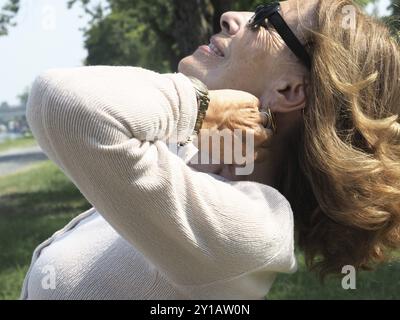 Eine Seniorin genießt einen sonnigen Tag im Park mit geschlossenen Augen, sonnigem Sonnenlicht, strahlt Zufriedenheit und Entspannung aus Stockfoto