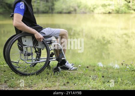 Glücklicher und junger behinderter Mann, der in der Natur auf einem Rollstuhl sitzt Stockfoto