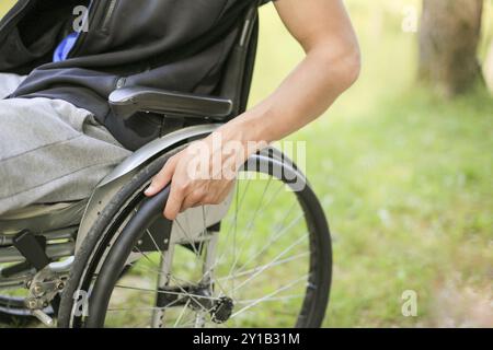 Junger behinderter oder behinderter Mann, der in der Natur auf einem Rollstuhl sitzt und Räder hält Stockfoto