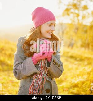 Junge lächelnde Frau mit Kaffeetasse in den Händen, die den Herbst genießt Stockfoto