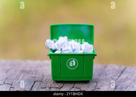 Nahaufnahme eines grünen Miniaturbehälters, gefüllt mit zerknittertem Papier, im Freien in einer natürlichen Umgebung. Stockfoto