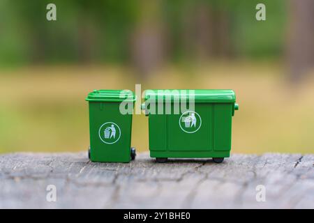 Zwei grüne Miniaturmüllbehälter, die im Freien auf einer Holzfläche platziert werden, fördern die Abfallbewirtschaftung und das Recycling. Stockfoto