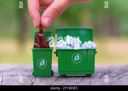 Händiges Abfüllen von Glasflaschen in einen grünen Miniaturbehälter für umweltfreundliche Recyclingverfahren. Stockfoto