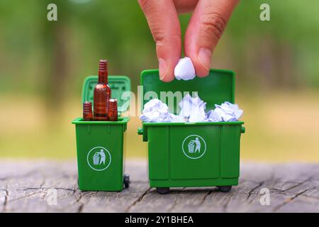 Eine Hand, die zerknittertes Papier in einen grünen Miniaturbehälter gibt, um die Bedeutung des Recyclings von Papierabfällen zu unterstreichen. Stockfoto