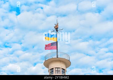 Kiew, Ukraine - 14. Oktober 2023: Leuchtende Fahnen der Ukraine und der USA winken auf einem Turm unter bewölktem Himmel und symbolisieren Einheit und Freundschaft. Stockfoto