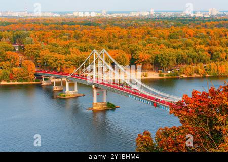 Kiew, Ukraine - 14. Oktober 2023: Blick auf die Fußgängerbrücke über den Fluss Dnieper in Kiew, umgeben von farbenfrohen Herbstlaub und ruhigem Wasser Stockfoto