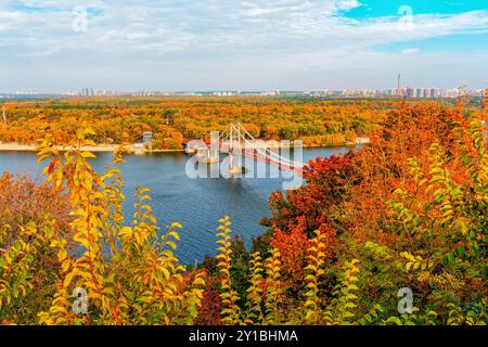 Kiew, Ukraine - 14. Oktober 2023: Blick aus der Vogelperspektive auf die Fußgängerbrücke über den Fluss Dnieper mit leuchtenden Herbstfarben und der Skyline der Stadt Stockfoto