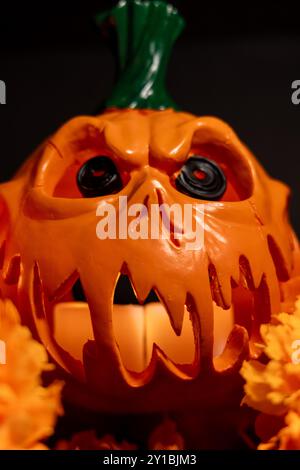 Ein vertikales Bild mit einem höhlen Halloween-Kürbis, der nach vorne blickt, mit Kerzen im Inneren, begleitet von einer beleuchteten roten Kerze und einer orangefarbenen Ringelblume Stockfoto