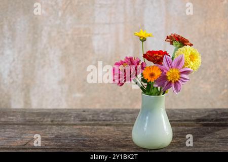 Blumenstrauß in einer Glasvase auf einem alten Holztisch vor einem flippigen Gipshintergrund Stockfoto