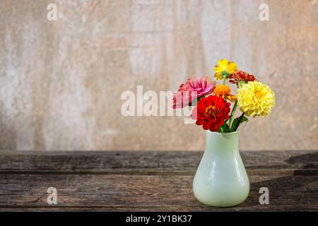 Blumenstrauß in einer Glasvase auf einem alten Holztisch vor einem flippigen Gipshintergrund Stockfoto