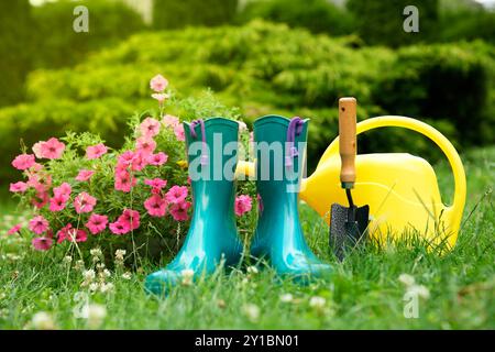 Gummistiefel, Gartengeräte und Petunienblüten auf grünem Gras im Freien Stockfoto