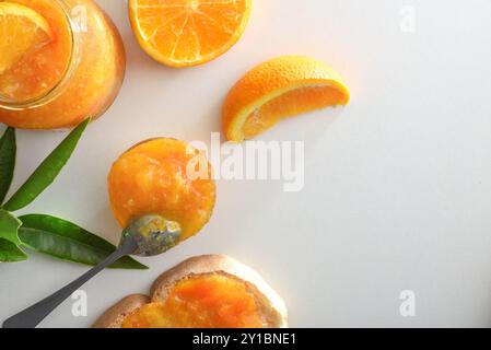 Gläser mit Orangenmarmelade isoliert auf weißem Tisch mit Früchten und Blättern. Draufsicht. Stockfoto