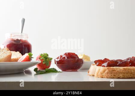 Frühstück mit Erdbeermarmelade mit Brotscheiben auf einer weißen Küchenbank und Küche im Hintergrund. Vorderansicht. Stockfoto