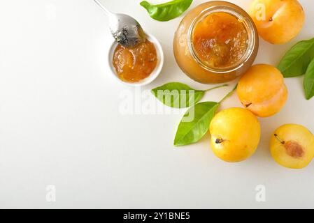 Gläser mit Pflaumenmarmelade isoliert auf weißem Tisch mit Früchten und Blättern. Draufsicht. Stockfoto