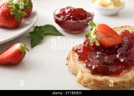 Frühstück mit Erdbeermarmelade und Brotscheibe auf einer weißen Küchenbank. Erhöhte Aussicht. Stockfoto