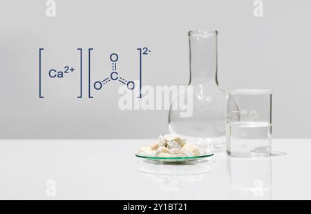 Calciumcarbonat-Chip in chemischem Uhrglas mit Molekularstruktur neben Becher und Flachbodenflasche auf weißem Labortisch. Seitliche Versiegelung Stockfoto