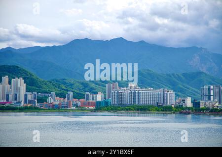 Sokcho, Südkorea - 28. Juli 2024: Ein breiter Blick auf die Skyline von Sokcho vor den zerklüfteten Taebaek Mountains mit dem ruhigen Wasser von Cheong Stockfoto