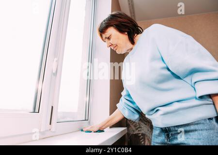 Active Seniors-Konzept. Hausfrau. Glückliche, Schüchterne Frau, Die Das Fenster Sauber Macht. Kaukasische Frau Im Mittleren Alter. Reinigungsappartement Für Ältere Frauen. Konzept Von Stockfoto
