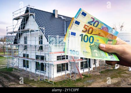 Handhaltung von Euro-Banknoten vor einem im Bau befindlichen Einfamilienhaus Stockfoto