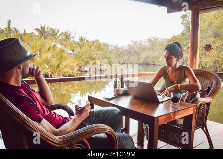 Nahaufnahme Hipster Digital Nomaden Paar sitzen im Café mit Laptop-Arbeit online am malerischen Fluss und Palmen in südostasien Stockfoto