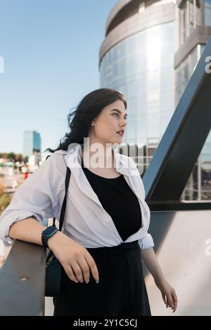 Moderne Eleganz: Stilvolle junge Frau posiert selbstbewusst vor einem futuristischen urbanen Hintergrund. Stockfoto