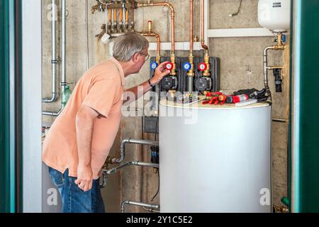 Technikraum einer Heizung, Teil einer neu installierten Wärmepumpenanlage, die eigentliche Wärmepumpe wurde draußen installiert, Glonn, Bayern, September 2024 Deutschland, Glonn, September 2024, Technikraum einer Heizung, Teil einer neu installierten Wärmepumpenanlage, die eigentliche Luft-Wärmepumpe steht draußen, hier im Keller befindet sich der Warmwasserspeicher für Heizung und Warmwasser und der Wärmetauscher verdeckt, links, Mann überprüft die Einstellungen, Rentner, die Anlage war erst vor zwei Tagen installiert, die Installation ist noch nicht abgeschlossen, Privathaus, Luftwärmepumpe Stockfoto