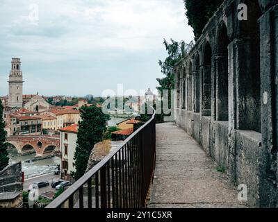 Schlendern Sie auf einem kopfsteingepflasterten Pfad mit Blick auf den Fluss, dieser Blick zeigt Verona atemberaubende Architektur und pulsierende Dächer während des späten A Stockfoto