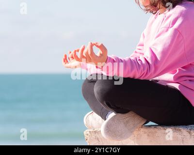 Person, die auf einem Felsvorsprung am ruhigen Meer meditiert Stockfoto