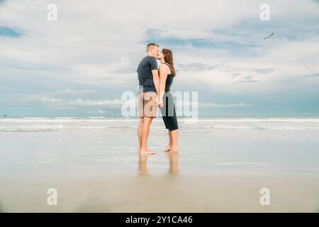 Paare küssen sich am Strand, halten Hände mit Reflektion in nassem Sand Stockfoto