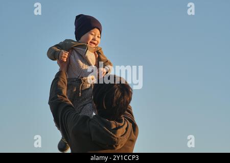 Vater hebt das Baby vor dem Hintergrund des klaren Himmels. Stockfoto