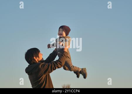 Vater hebt das Baby vor dem Hintergrund des klaren Himmels. Stockfoto