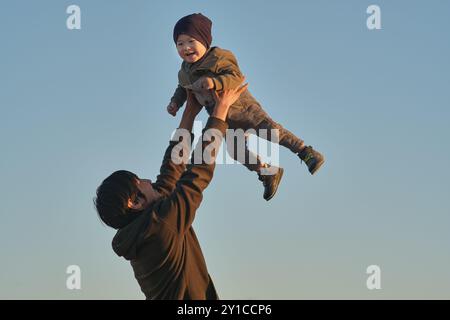 Vater hebt das Baby vor dem Hintergrund des klaren Himmels. Stockfoto