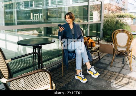 Glückliche junge Frau mit Smartphone im Café im Freien Stockfoto