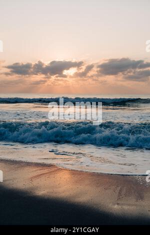 Goldener Sonnenaufgang über schaumigen Wellen, die sich am Sandstrand spiegeln. Stockfoto