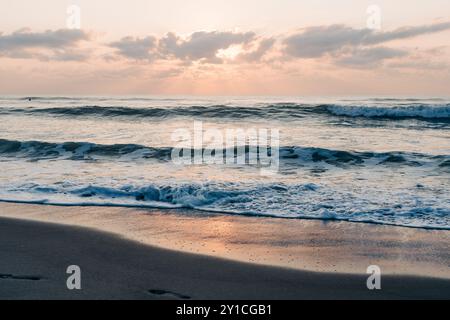 Goldener Sonnenaufgang am Ufer mit sanften Wellen und weichen Wolken Stockfoto