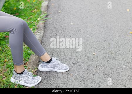 Asiatische Frau sitzt nach langen Strecken auf der Straße und fühlt sich müde vom Laufen und Pausen, um Laufverletzungen zu reduzieren Stockfoto