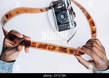 Nahaufnahme afrikanischer Mannhände, die 35-mm-Filmband vor dem Hintergrund einer alten Kamera halten. Alte klassische analoge Fotografie mit isolierten Negativen. Man wählt Rahmen aus und überprüft die Qualität Stockfoto