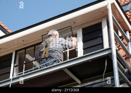 Bauarbeiter, der neues Glas in ein Fenster mit Stabteilung eines älteren Hauses einbaut. Renoviertes Haus mit Doppelverglasung Stockfoto