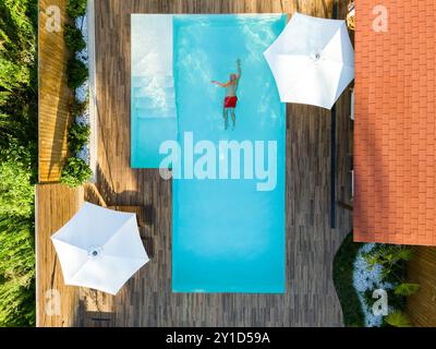 Mann schwimmt allein im Pool der Luxusvilla. Draufsicht aus der Luft. Bild des unvorsichtigen Sommerurlaubs Stockfoto