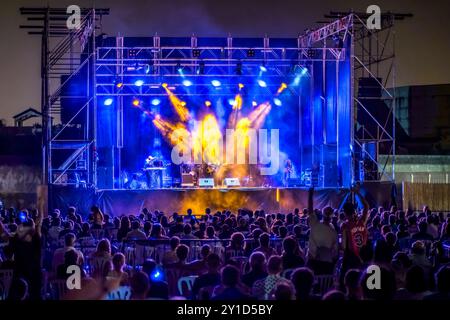 Ein aufregendes abendliches Rockkonzert mit einem großen, energiegeladenen Publikum, das Live-Musik unter farbenfrohen Bühnenlichtern genießt. Die Atmosphäre ist lebendig und flink Stockfoto