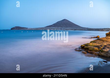 Langzeitfoto der Costa de El Medano mit Montana Roja im Hintergrund während der Dämmerung, Granadilla de Abona, Teneriffa, Kanarische Inseln, Spanien. Stockfoto