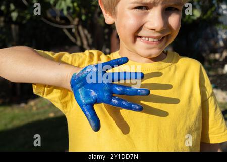 Der Junge in einem gelben T-Shirt zeigt seine Hand blau bemalt und schafft so die Flagge der Ukraine. Unabhängigkeitstag der Ukraine. Patriotisches Konzept. Kinder aus Großbritannien Stockfoto