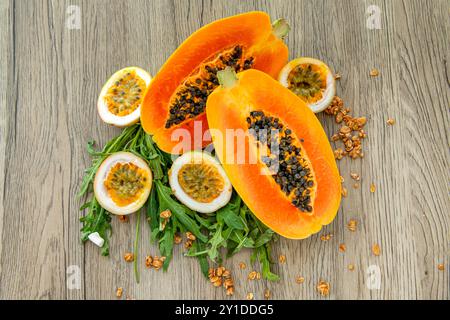 Papaya-Frucht, Passionsfrucht, Rucola und Müsli auf hellem hölzernem Hintergrund. Scheiben süßer Papaya, Maracuja, grüner Rucola umgeben von Granola fla Stockfoto