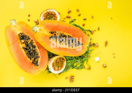 Papaya, Passionsfrucht, Rucola und Müsli auf gelbem Hintergrund. Scheiben von süßer Papaya, Passionsfrucht, Rucola umgeben von Granola Flocken auf Gelb Stockfoto